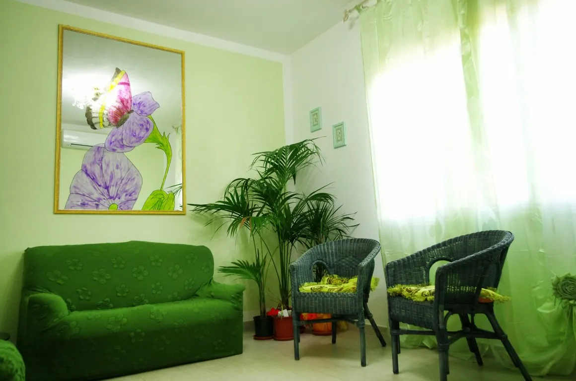 Sala d'attesa dello studio con divano verde, piante e quadro floreale